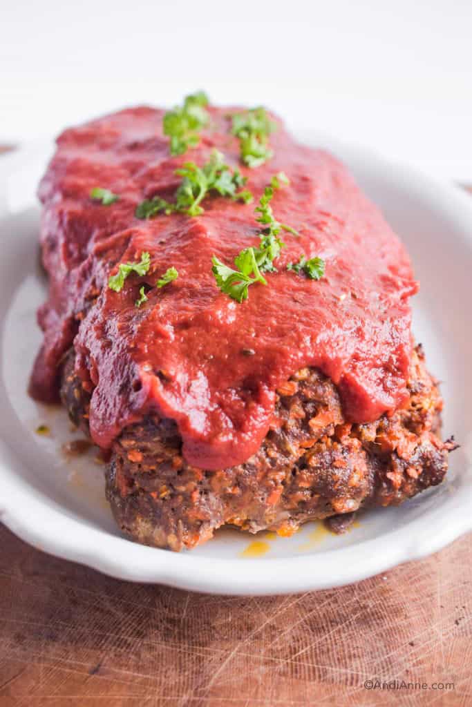 keto vegetable meatloaf with sauce and parsley on top. In a white dish.