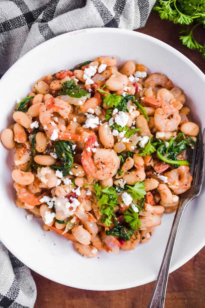 shrimp, white kidney beans onions, feta cheese and shrimp in a white bowl with a silver spoon.