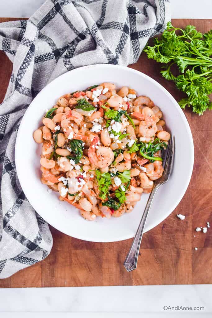 shrimp one pot dinner in a white plate with a fork. Parsley and a kitchen towel surround it.