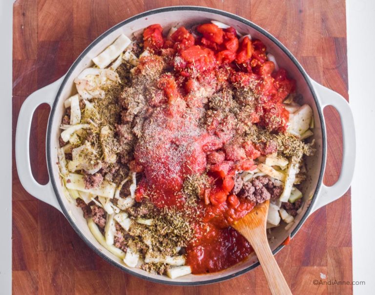 shredded cabbage, ground beef, diced tomatoes, sauce and spices in white pan with wood spatula.