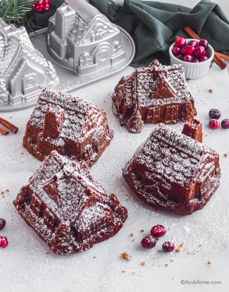 four gingerbread house cakes sprinkled with powdered sugar with nordic ware gingerbread cake duet pan in background