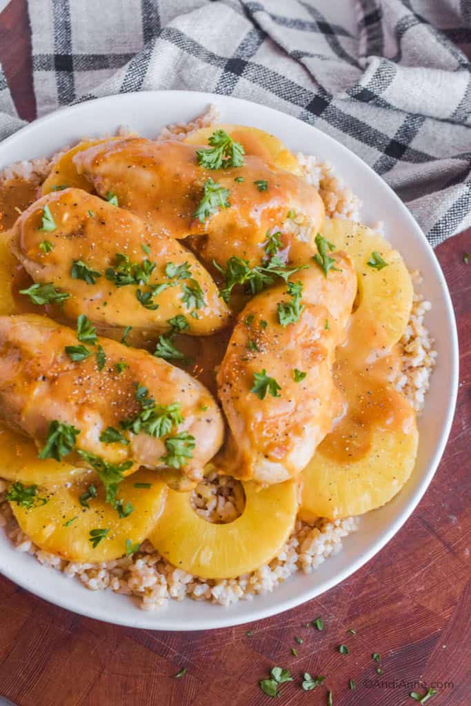 Plate of cooked chicken breasts with pineapple slices and rice with kitchen towel in background.