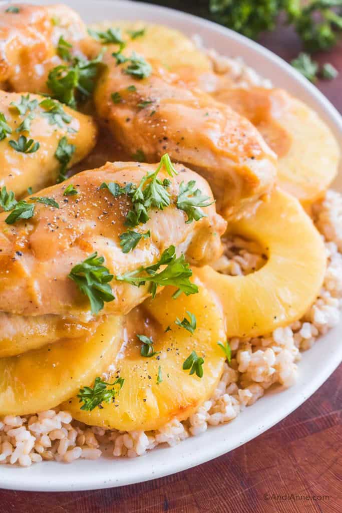 Close up of pineapple chicken with rice and chopped parsley on a white plate.