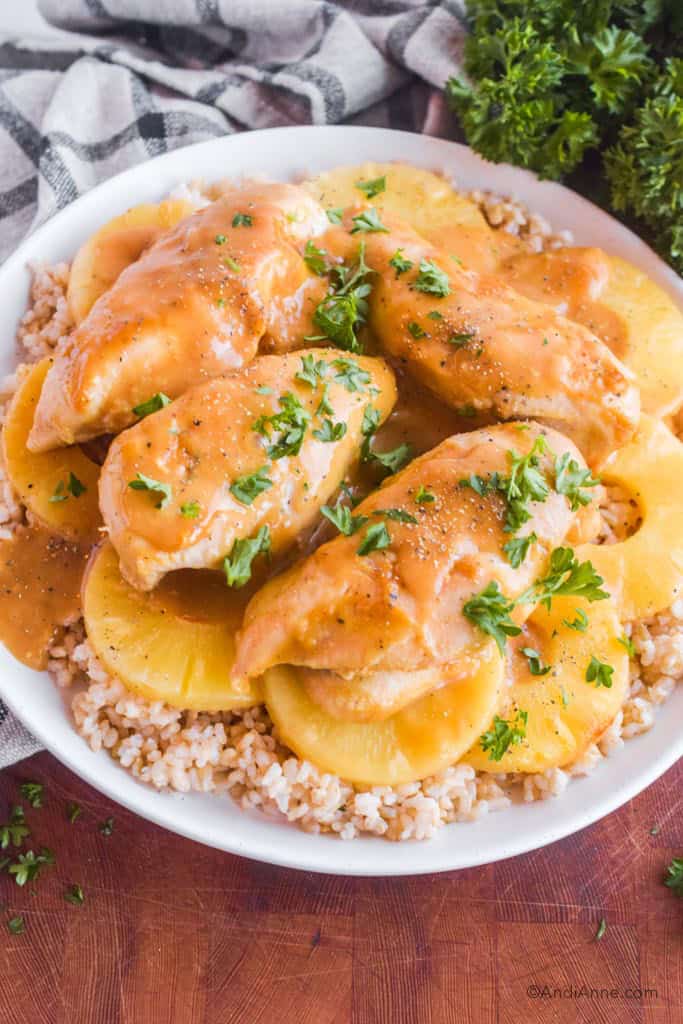 Plate of cooked pineapple slices, chicken breasts, and rice. Sauce drizzled over top and parsley sprinkled.