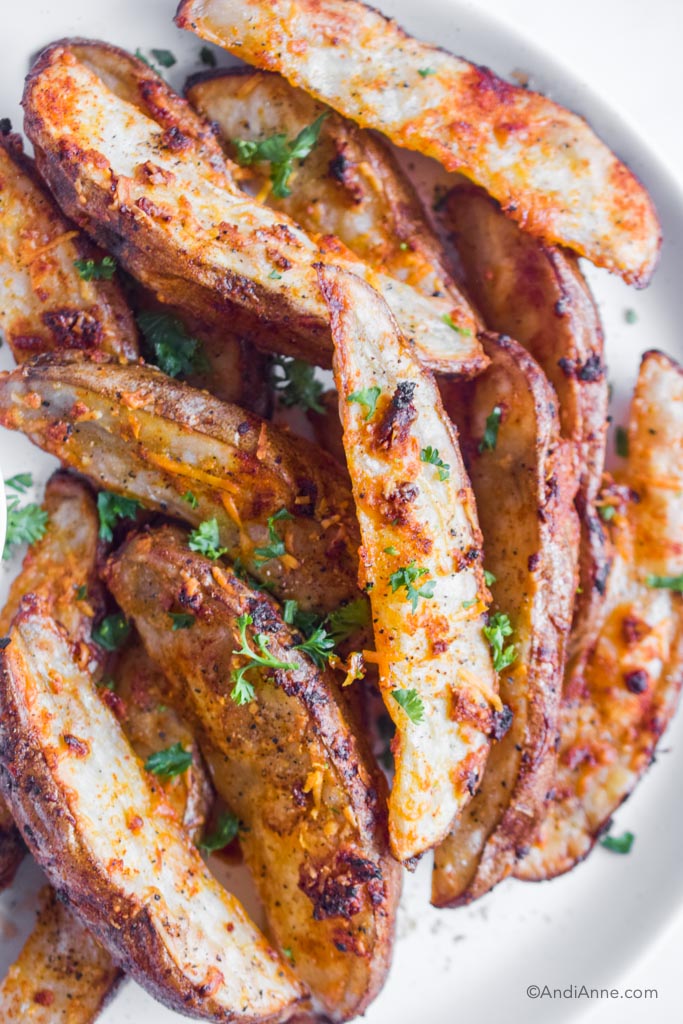 close up of crispy potato wedges with chopped parsley sprinkled on top.