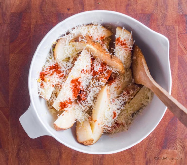 potato wedges with parmesan and paprika in white bowl with wood spoon