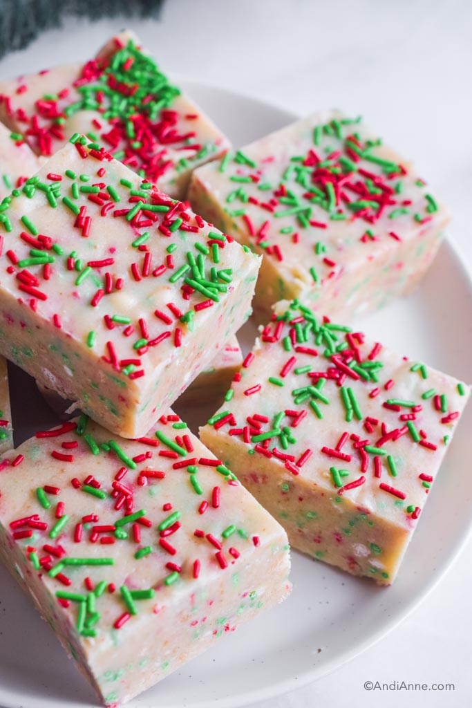 Squares of holiday christmas fudge on white plate with red and green sprinkles. 
