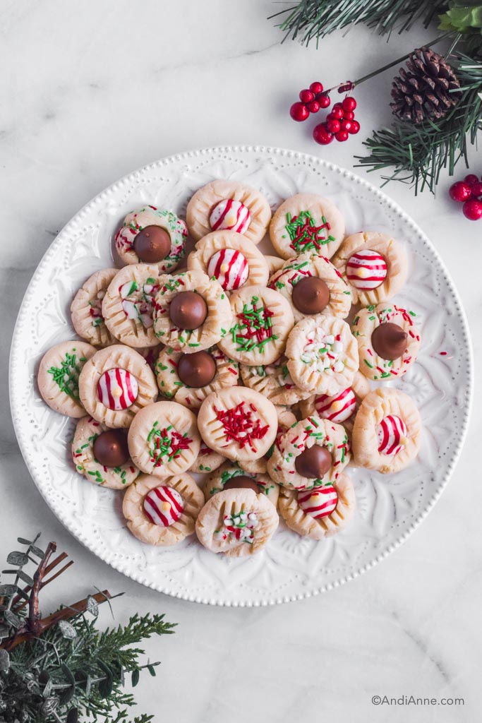 A white plate of christmas whipped shortbread cookies with candy decorations. Christmas greenery in corners of photo.