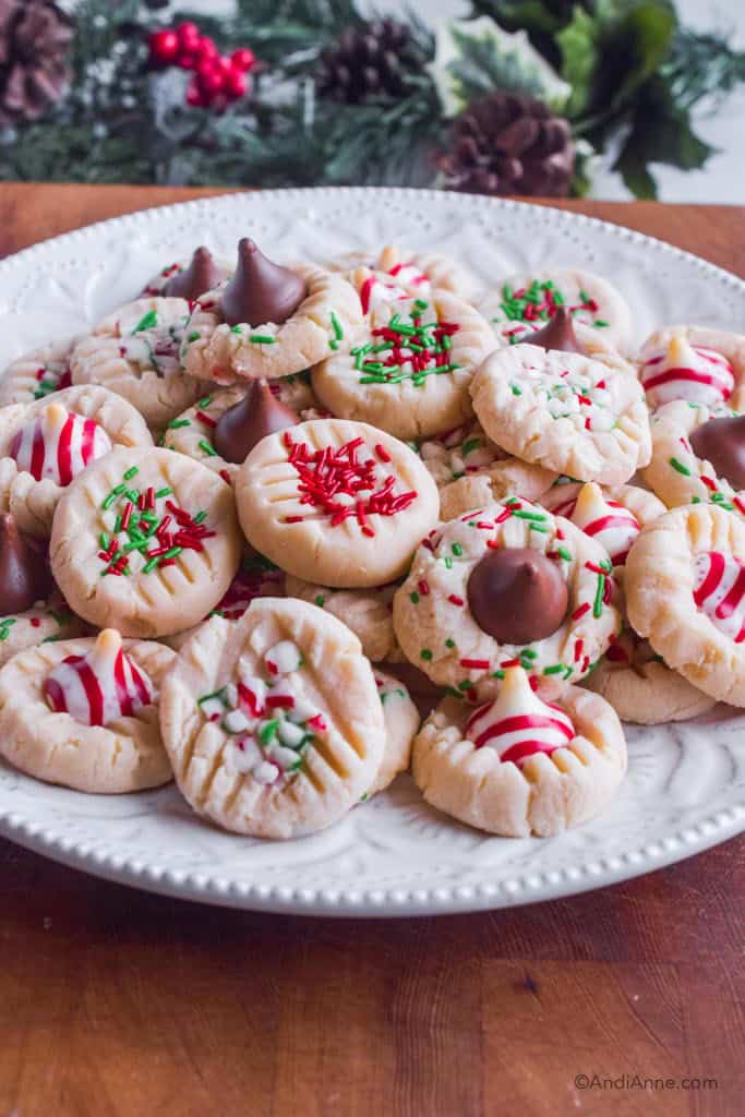 Pile of christmas shortbread cookies on white plate with greenery in background.