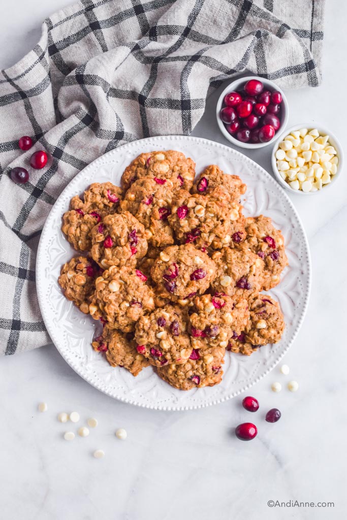 Looking down at a plate of oatmeal cranberry cookies with chocolate chips, fresh cranberries and a kitchen towel surrounding plate.