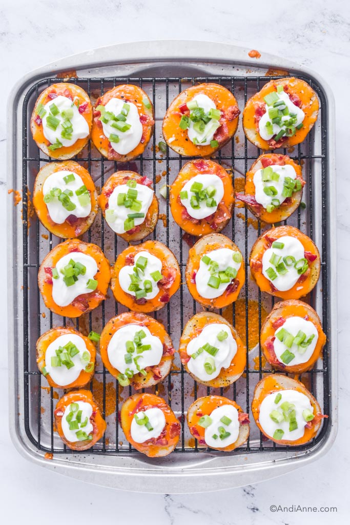 Looking down at baking rack with bacon cheddar potato slices with sour cream and green onion on top.