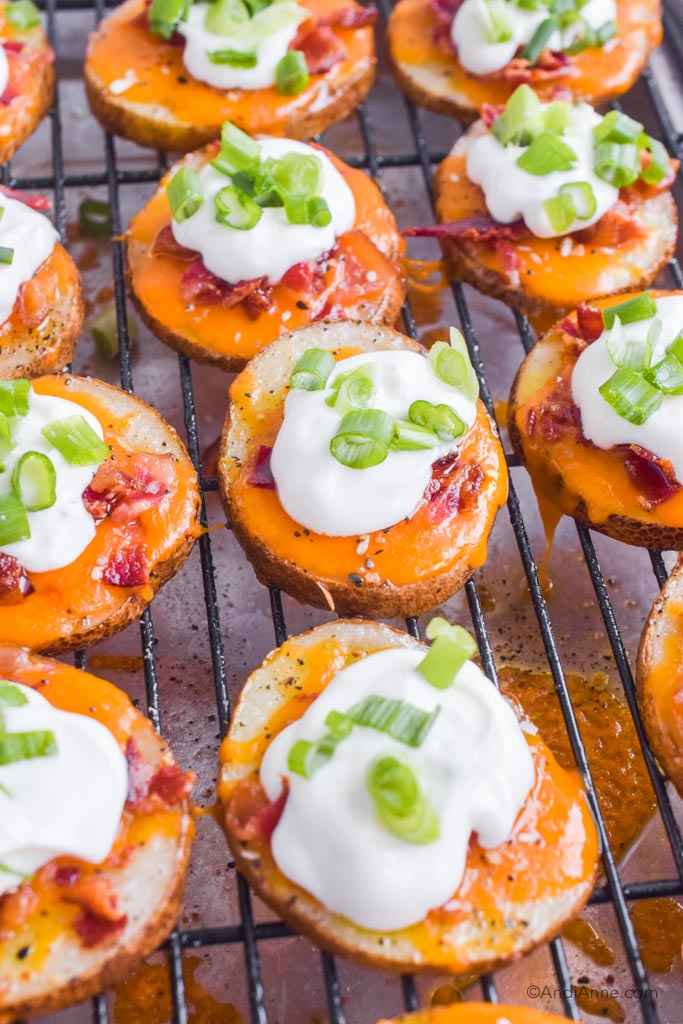bacon cheddar potato skins with sour cream and green onion pieces on top. Sitting on baking rack.