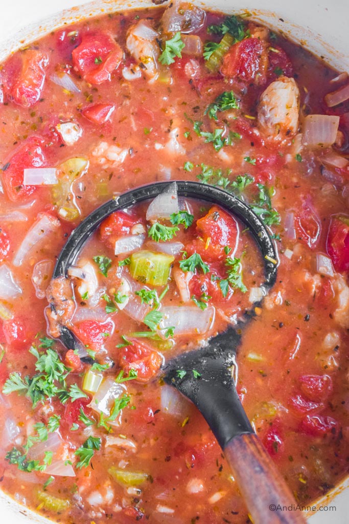 Close up of soup spoon in pot of tomato cod soup