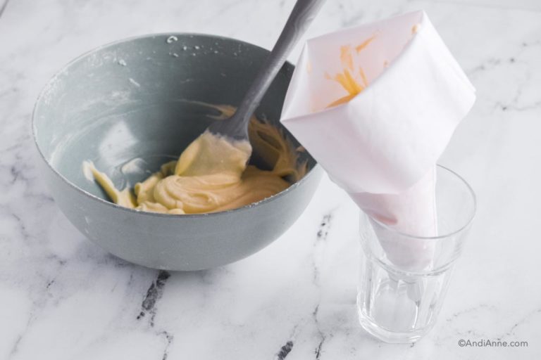 bowl of frosting with spatula and white piping bag sitting in tall glass
