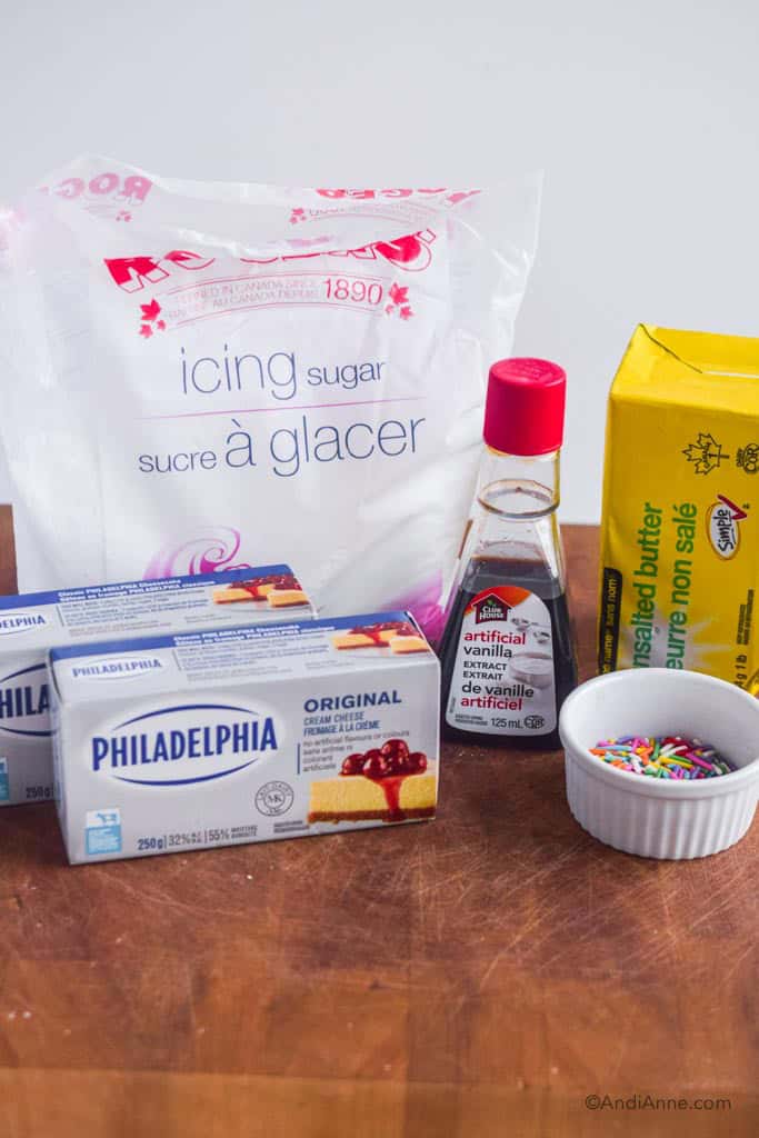 Ingredients on counter including icing sugar, cream cheese, butter, artificial vanilla extract and jimmies sprinkles.