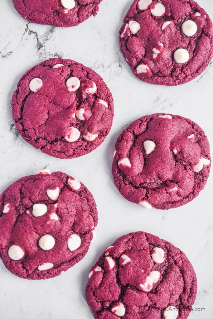 six red velvet cake mix cookies with white chocolate chips on white marble counter.