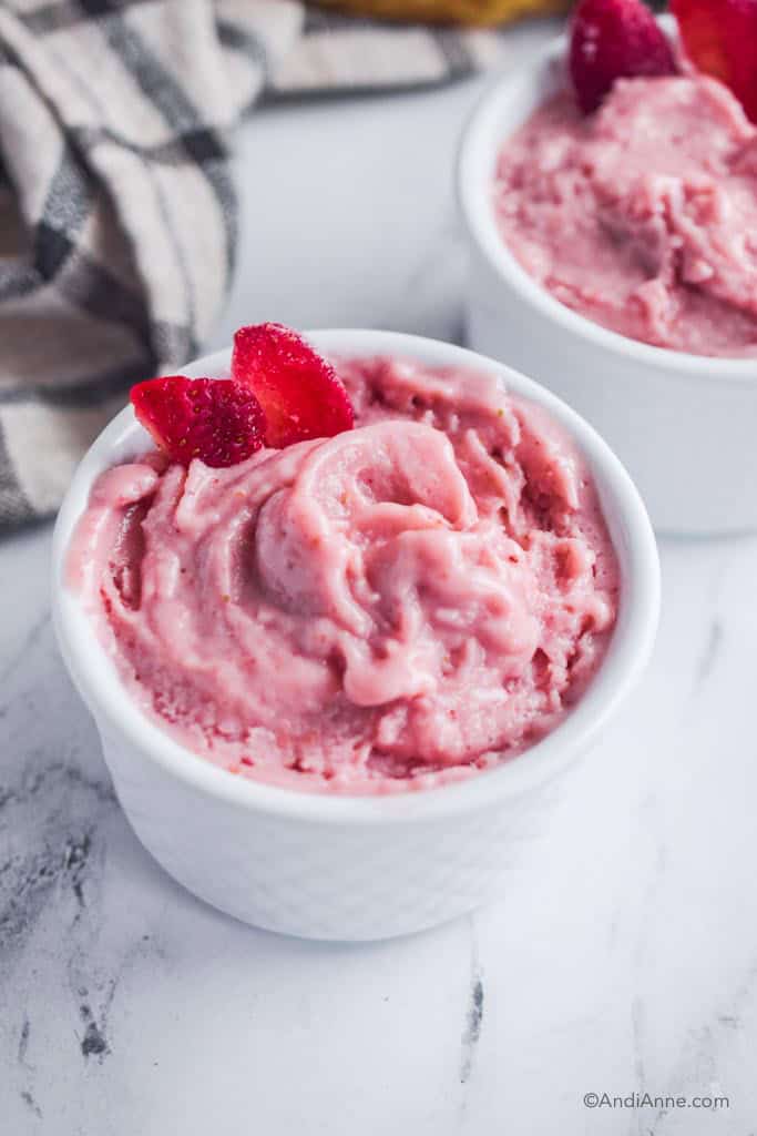 Close up of strawberry banana nice cream in white bowl with two frozen strawberries placed in.
