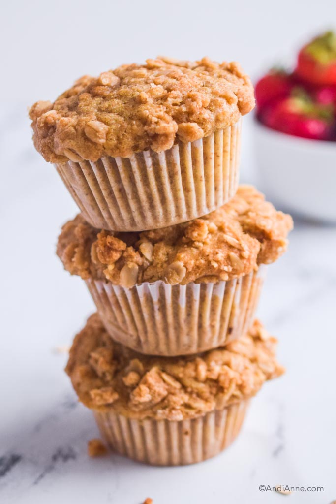 three buttermilk streusel muffins stacked on top of eachother with bowl of strawberries in background