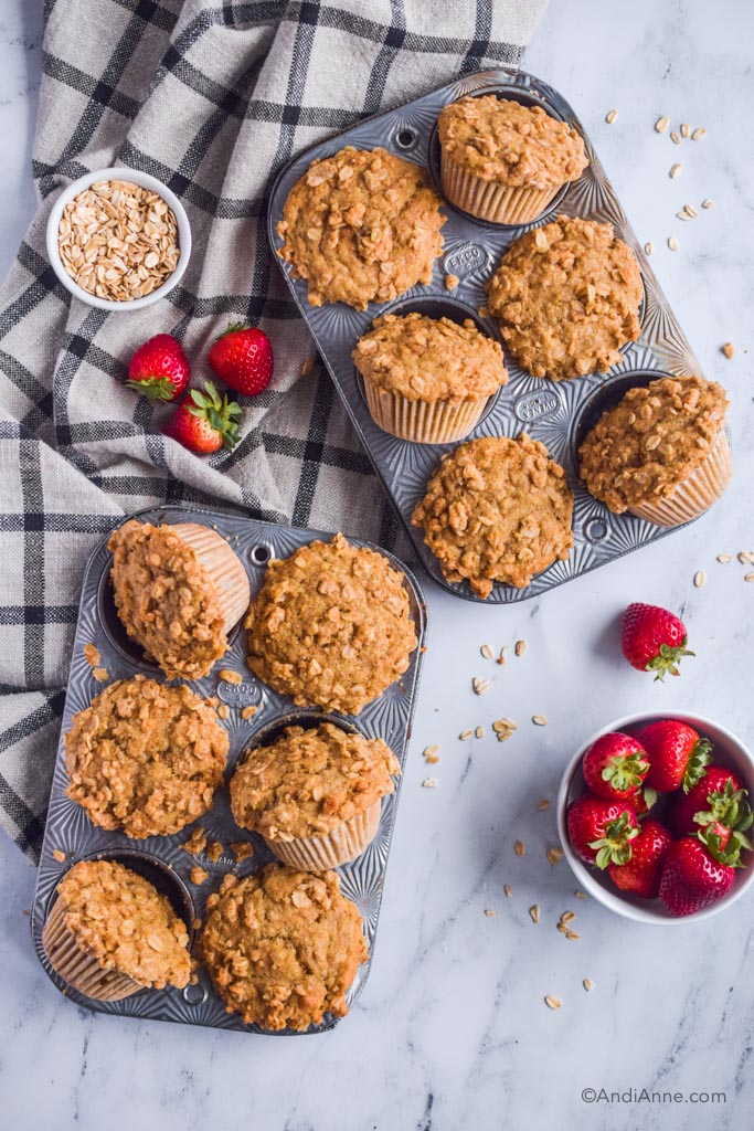 whole wheat buttermilk streusel muffins in old ecko baking pans. Kitchen towel, small bowl of oats, bowl of strawberries beside muffin pans.