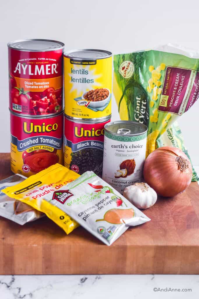 Ingredients for soup on counter: canned tomatoes, crushed tomatoes, lentils, black beans, coconut cream, corn, onion, garlic, and bags of spices.
