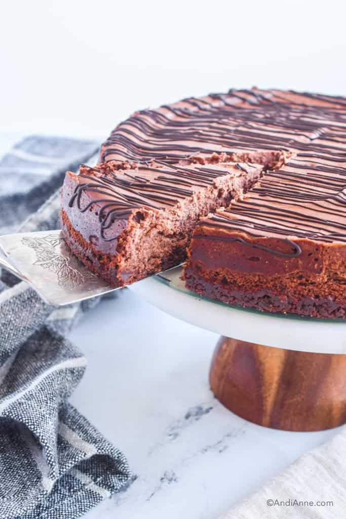 Slice cut out of chocolate cheesecake on cake stand. Pie server removing the slice.