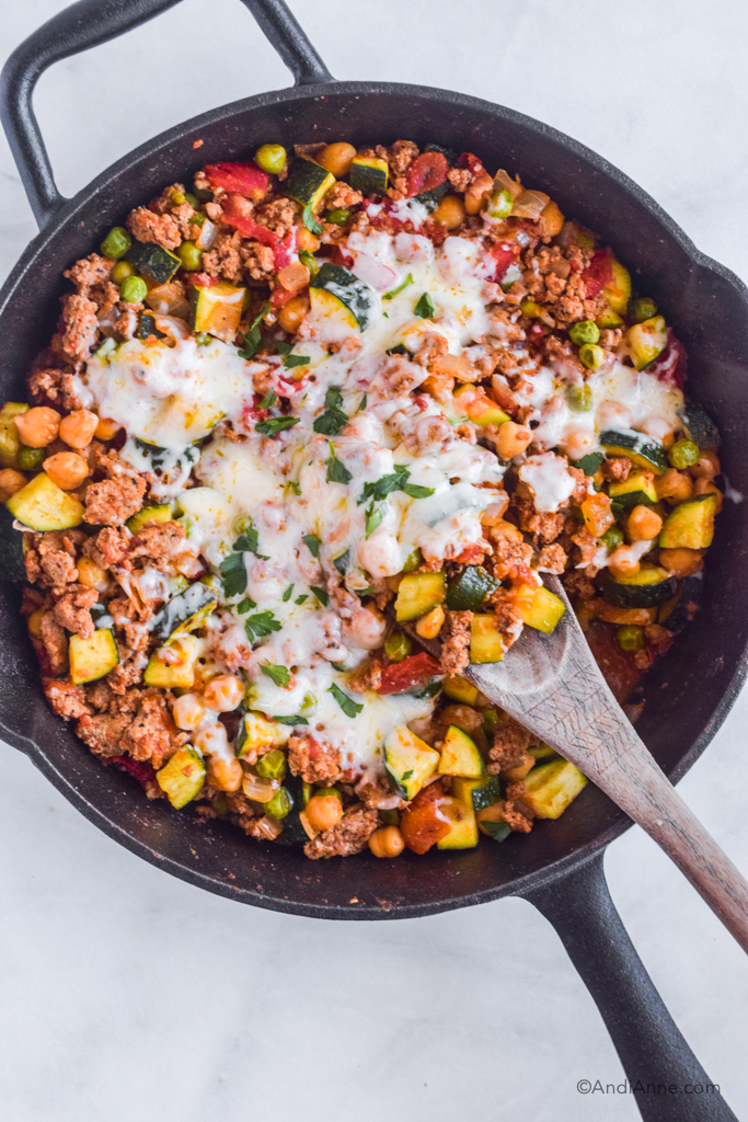 Wood spoon in frying pan with ground turkey zucchini chickpea recipe with melted mozzarella cheese on top.