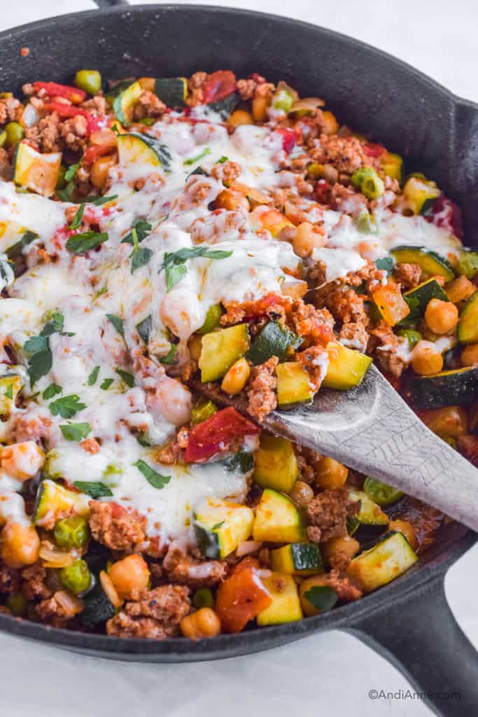Ground turkey zucchini chickpea skillet recipe with melted mozzarella cheese. Wood spoon scooping some ingredients.