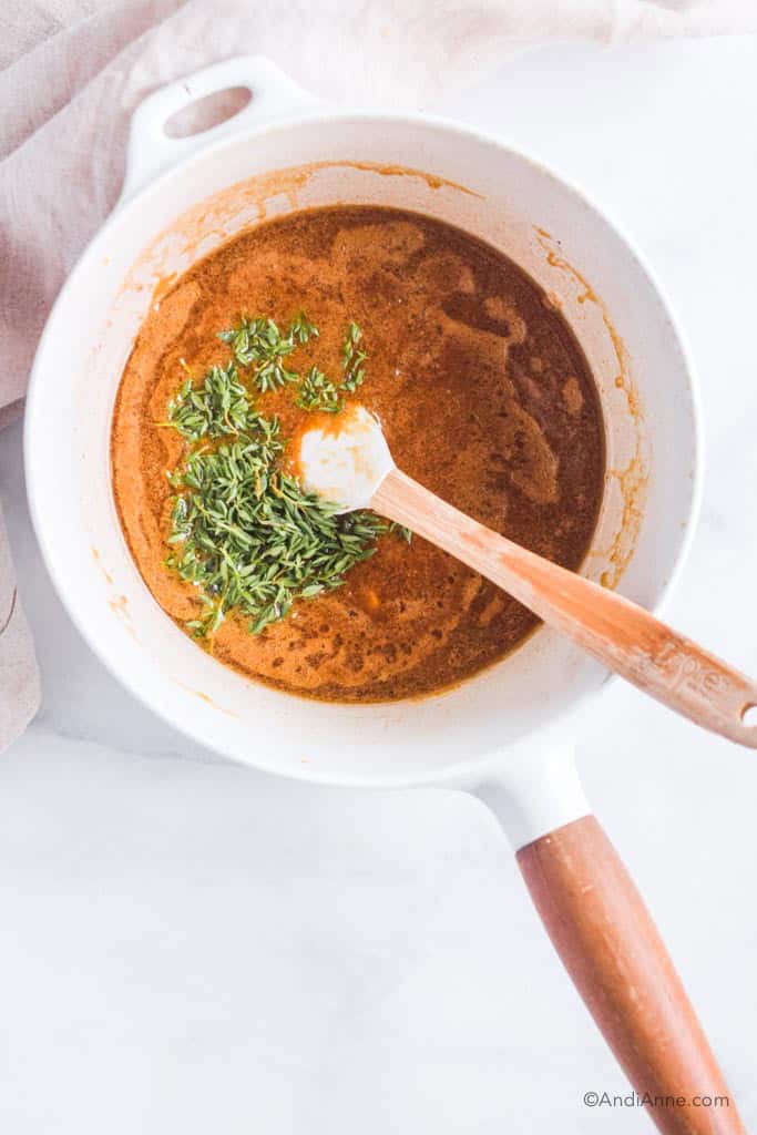 White pot with wood handle and honey mustard sauce inside. Fresh thyme and small wood spatula also inside.