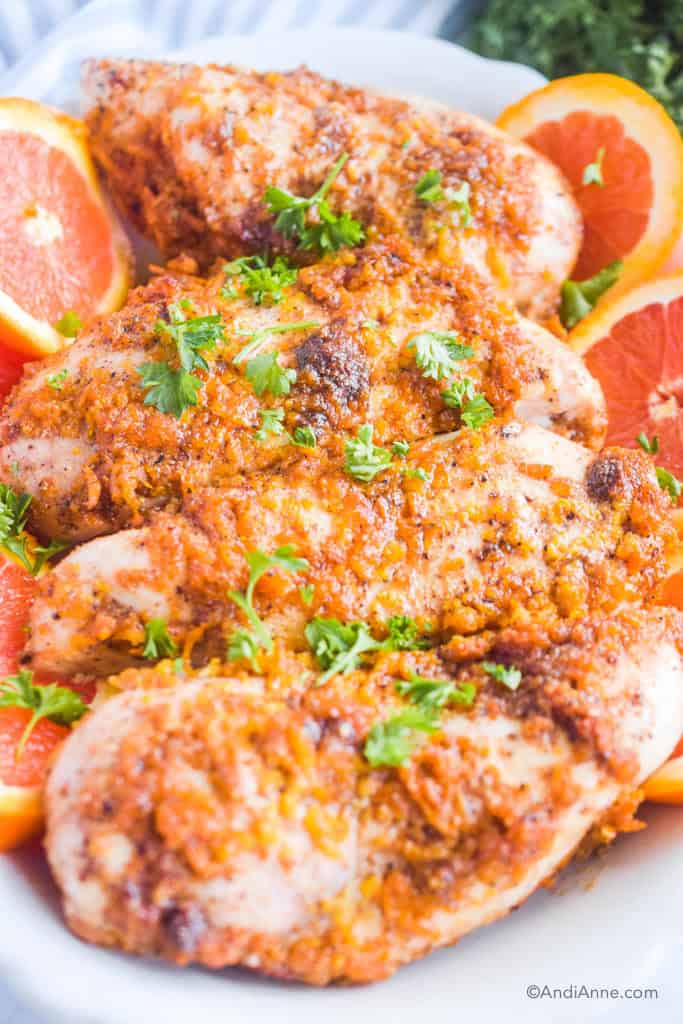 Baked orange ginger chicken breasts with slices of orange beside it and fresh parmesan sprinkled on top.