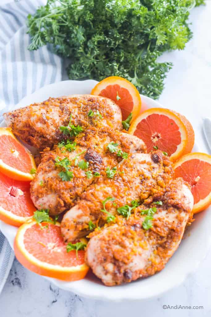 Honey orange chicken breasts on plate with slices oranges. Fresh bunch of parsley and kitchen towel in behind it.