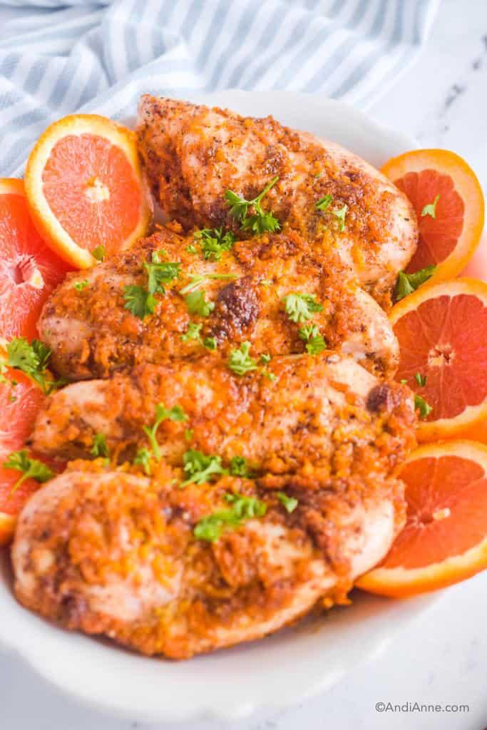 Close up of chicken breasts with sliced oranges and orange sauce. Striped towel in background.