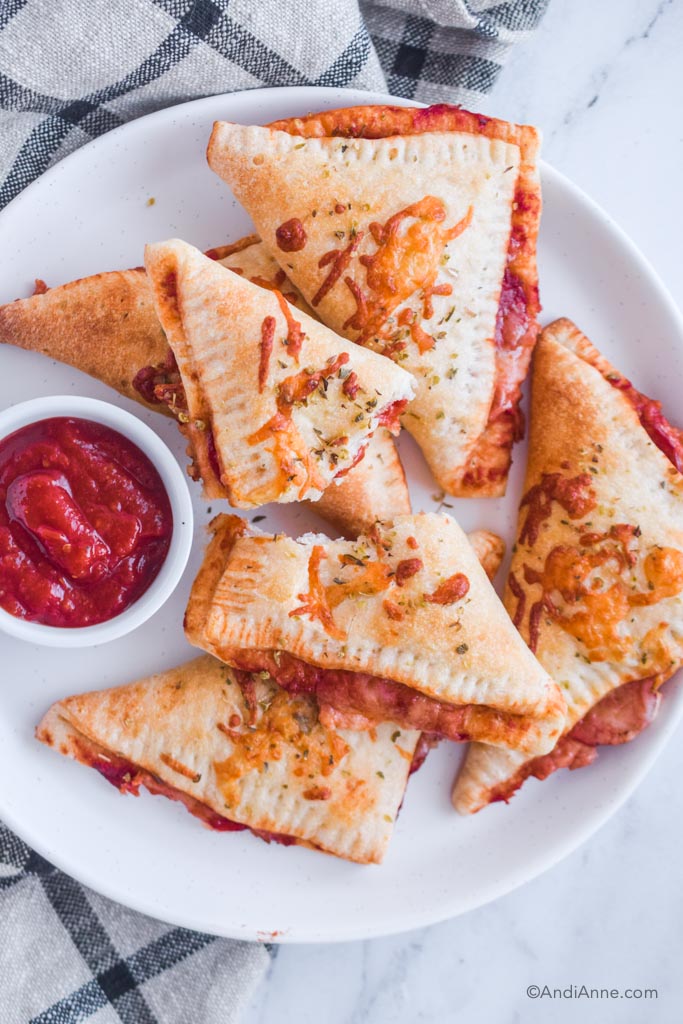 homemade pizza pockets stacked on a plate with small bowl of pizza sauce.