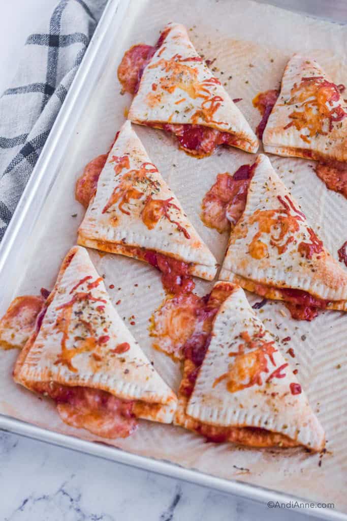 six homemade pizza pockets on a baking sheet with cheese and sauce oozing out of them