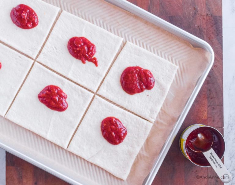 pizza dough squares with pizza sauce dolloped on each