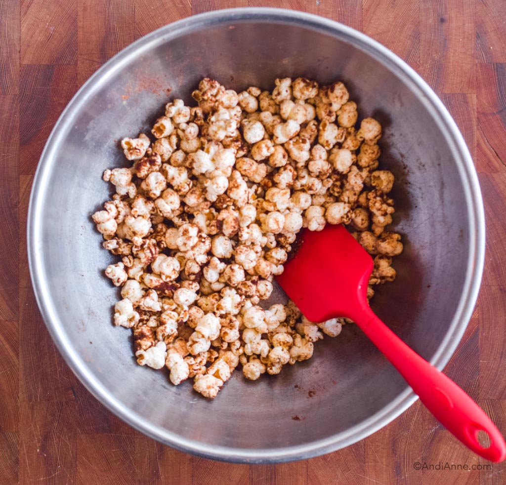 Steel bowl with popcorn and spices mixed together and red spatula.