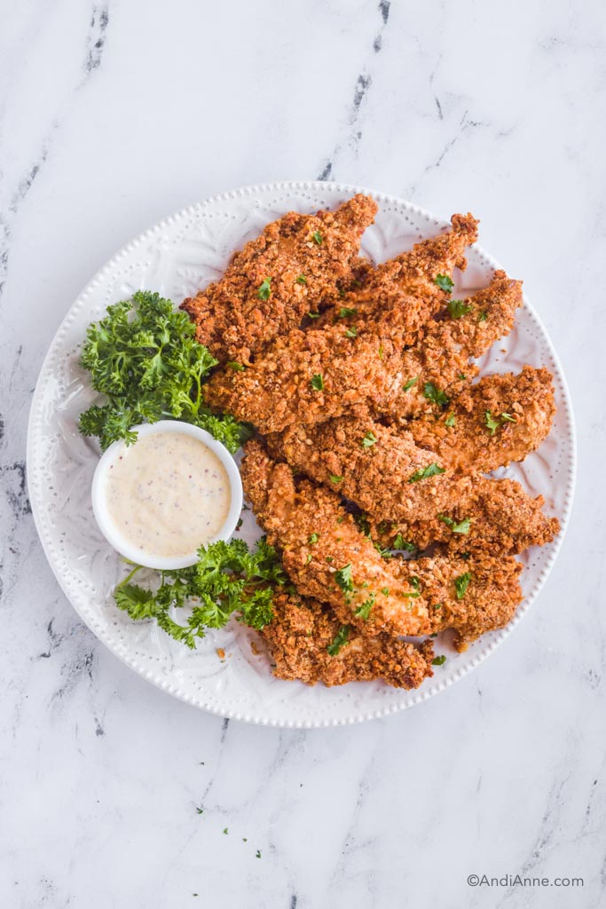 looking down and white plate of pretzel chicken tenders with parsley and small bowl of dipping sauce