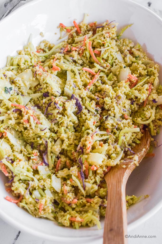 close up of avocado quinoa coleslaw in a white bowl with wood spoon
