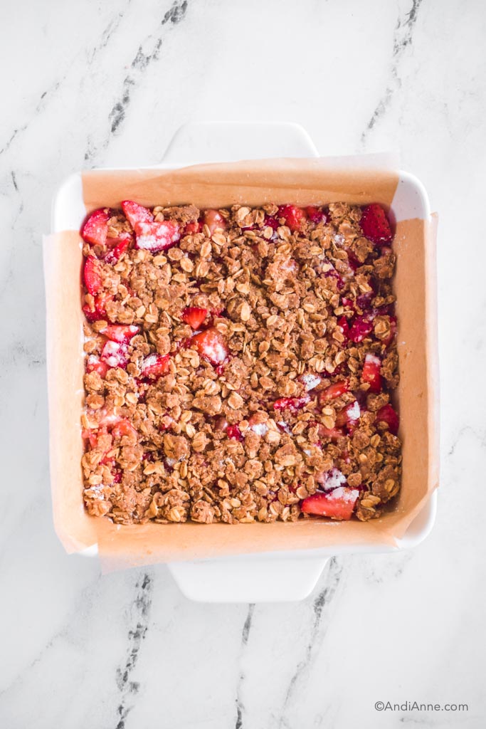 white dish of baked strawberry oatmeal bar recipe with parchment paper.