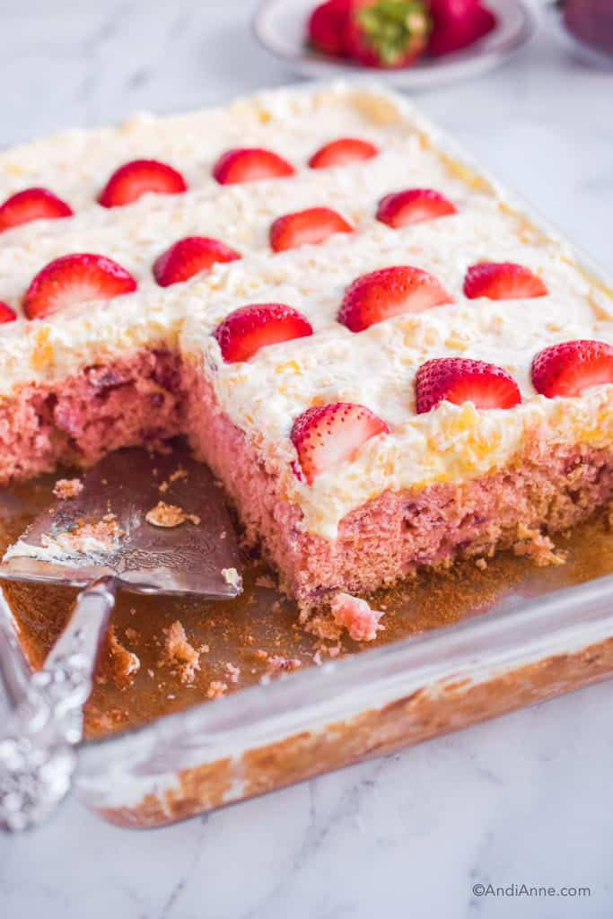 strawberry pineapple cake with slices cut out and silver pie server. Plate of strawberries in background.