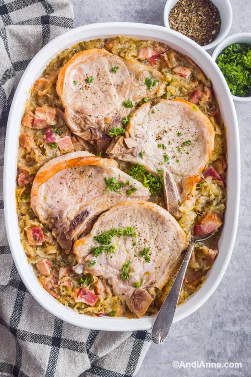 Looking down at pork chops on top of sauerkraut with bacon in casserole dish. Spoon scooping out some of recipe.