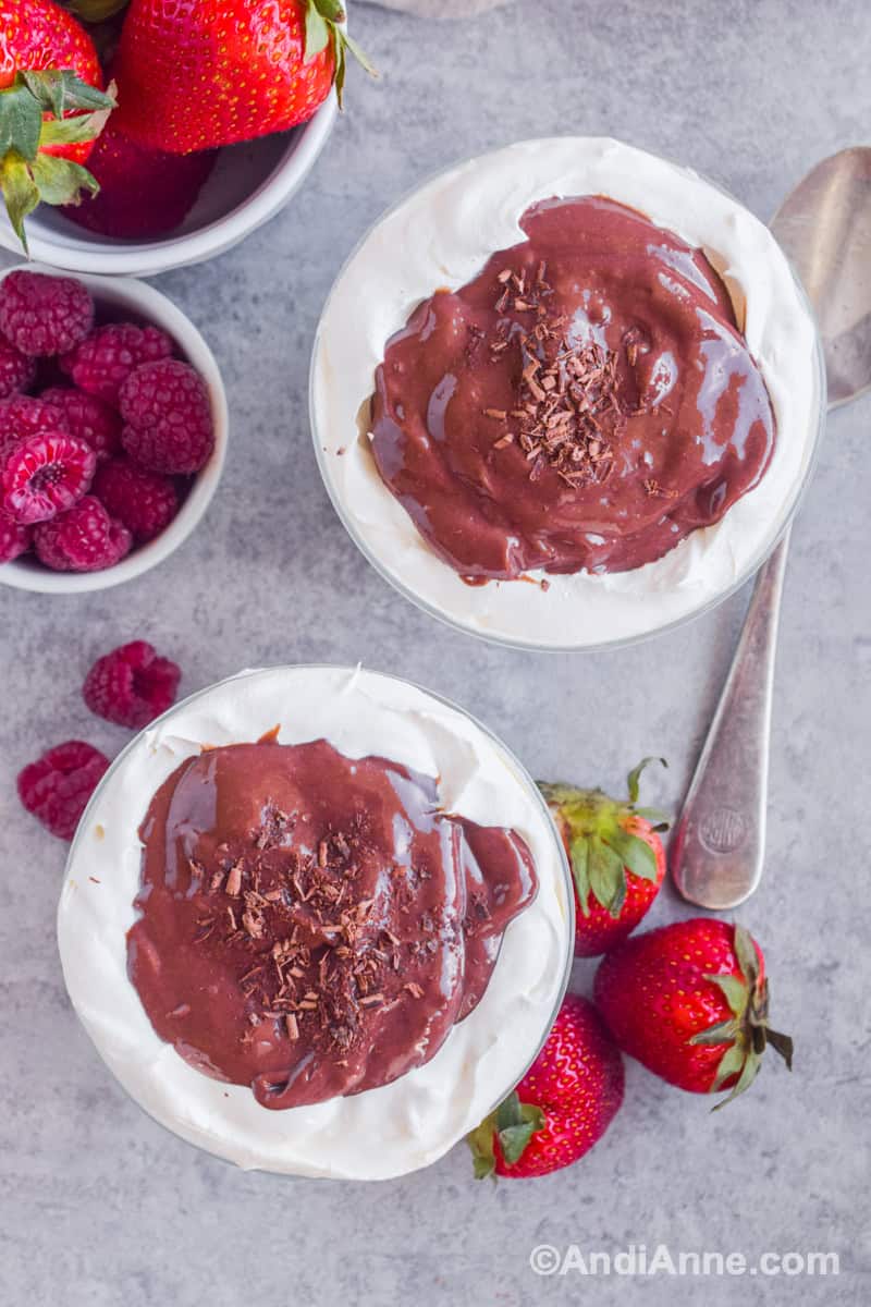 Looking down at whipped topping and chocolate pudding in two dessert cups. Fresh raspberries and strawberries surround them.