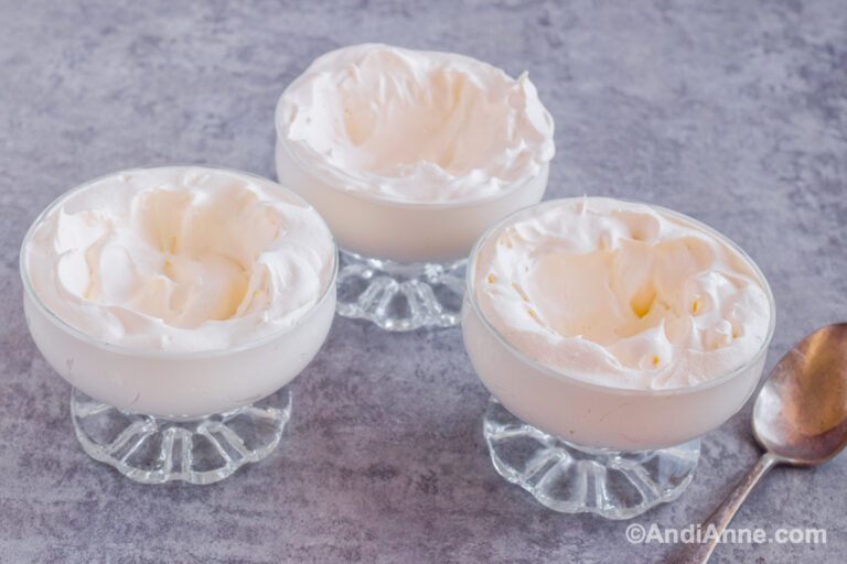 Three glass dessert dishes with whipped cream and a spoon beside.