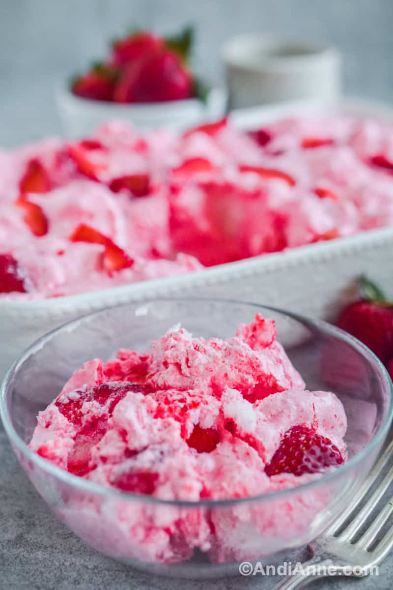 Close up of whipped strawberry dessert in glass bowl with a fork beside and full dessert dish blurred in background.