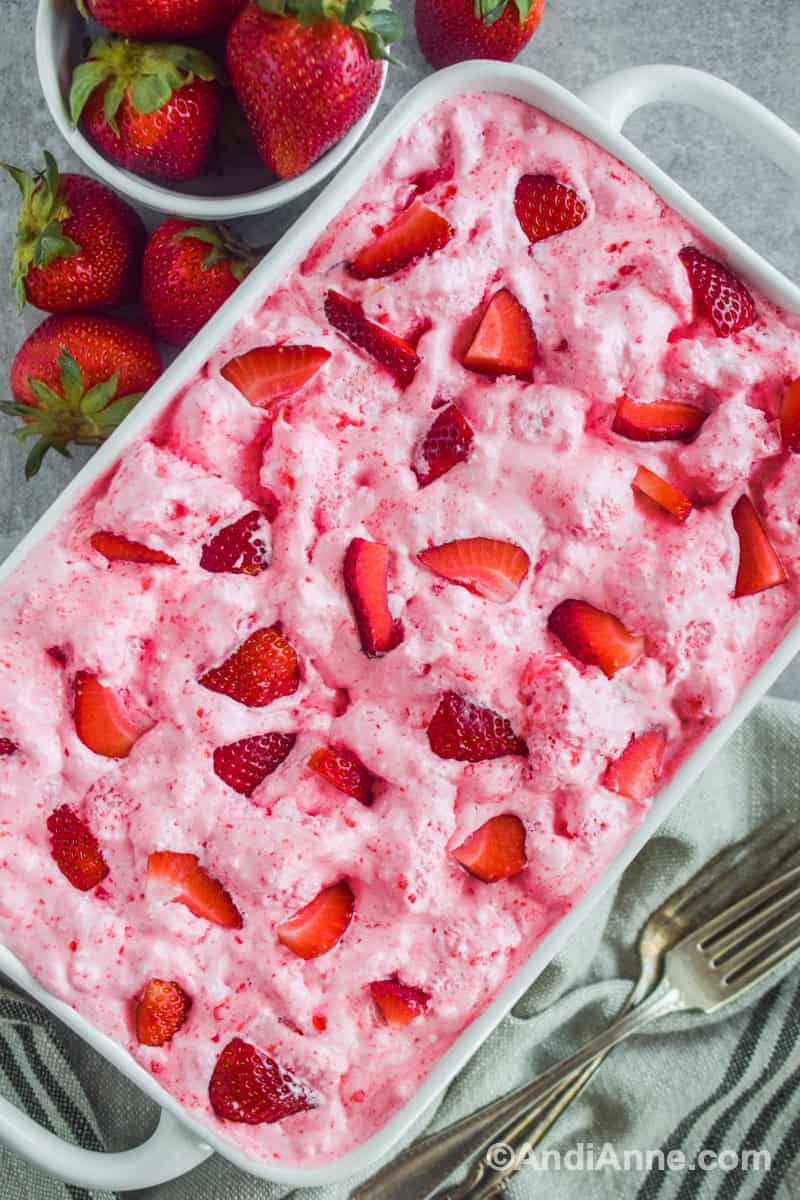 Strawberry angel food dessert in white casserole dish with forks and strawberries surrounding it.