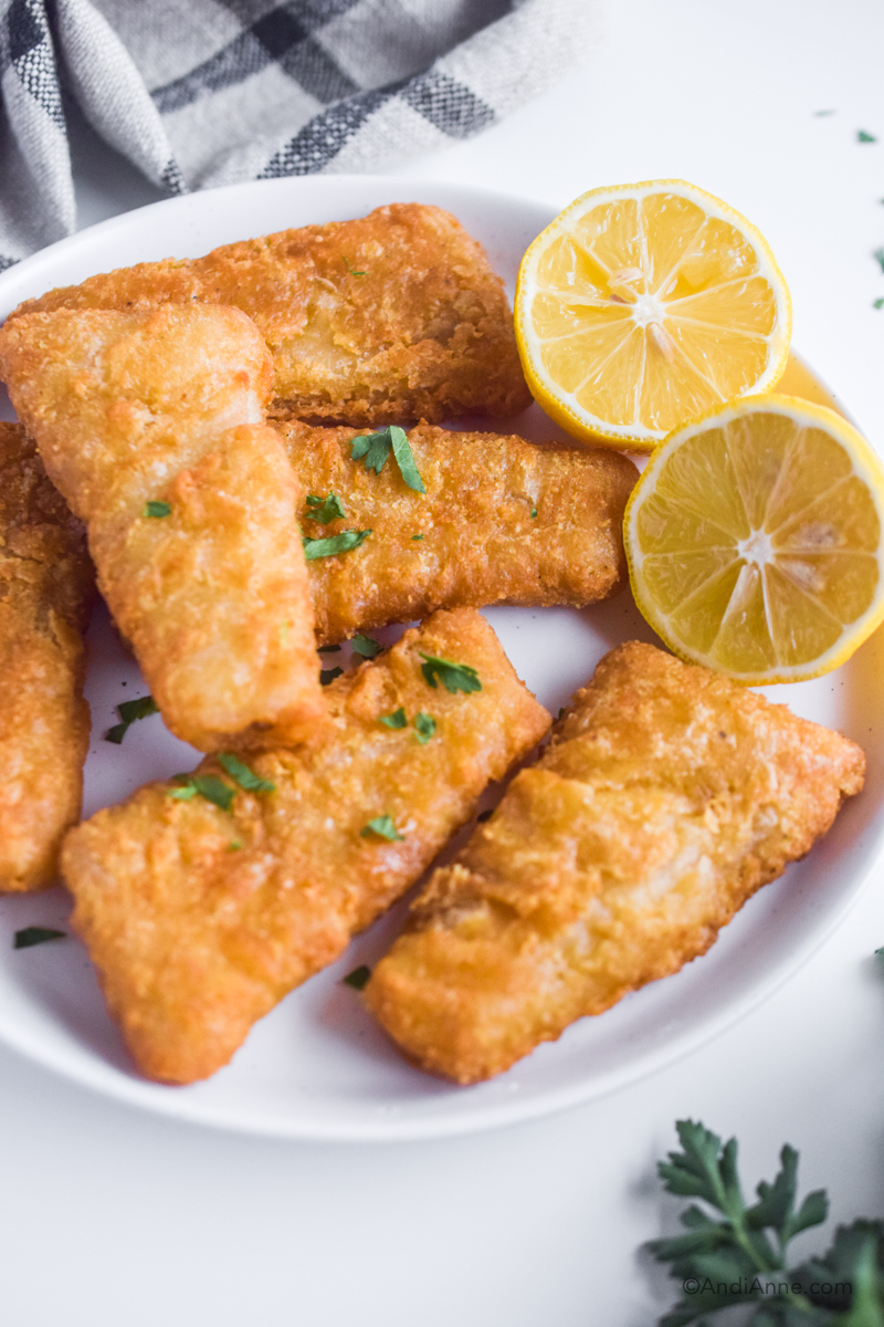 Close up plate of fish sticks with sliced lemon .