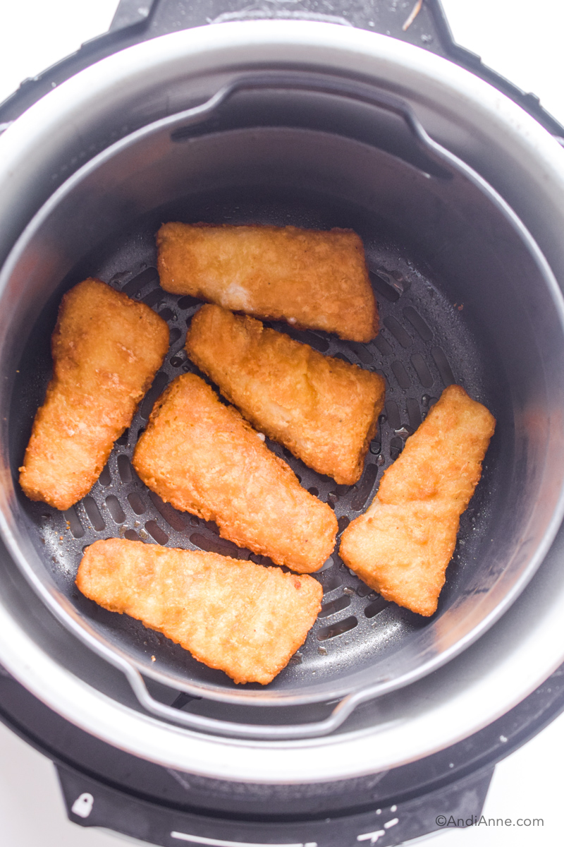 Looking down at frozen fish sticks in an air fryer. 