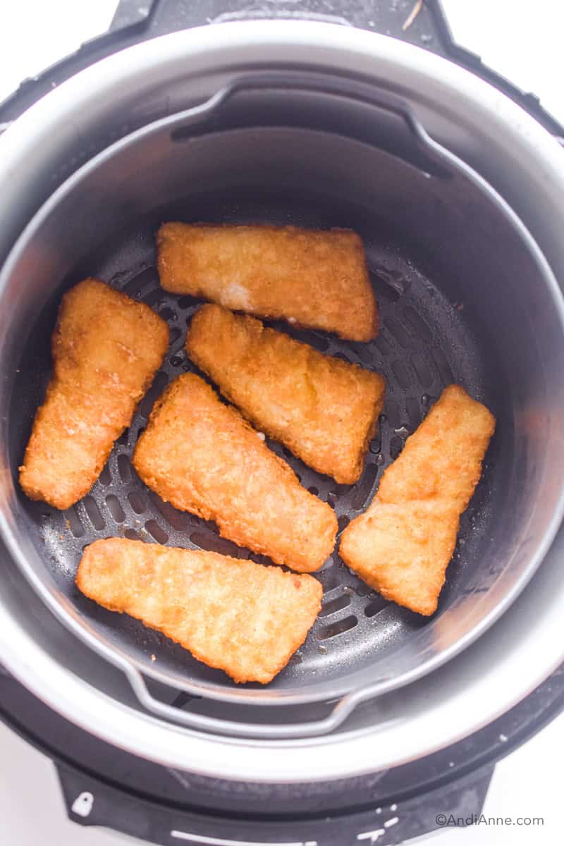 Looking down at frozen fish sticks in an air fryer.