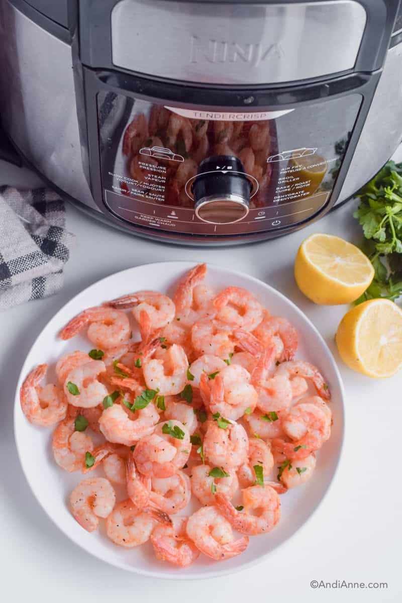 White plate of air fried shrimp with sliced lemon and ninja foodi deluxe air fryer in background.