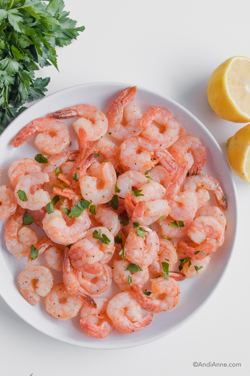 White plate with cooked shrimp, sliced lemon and fresh parsley beside the plate.