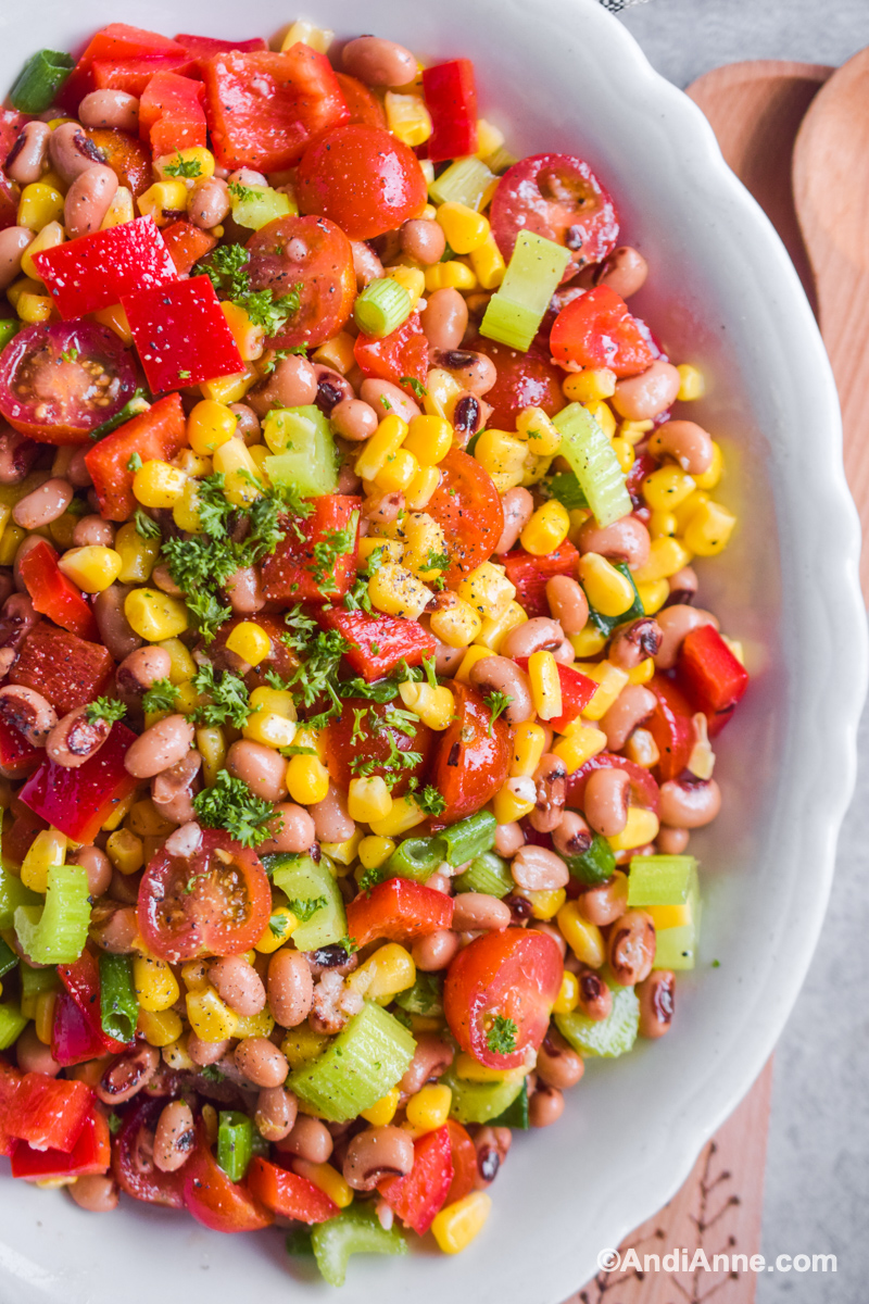 Close up of finished salad with cherry tomatoes, corn, celery and bell peppers. Top of salad is sprinkled with chopped parsley.
